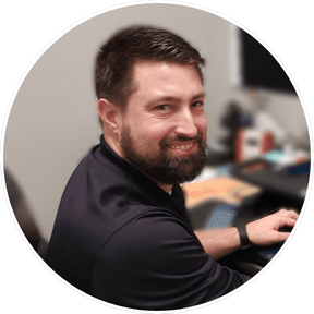 A circular photo of a man with dark hair and a beard, smiling at the camera.