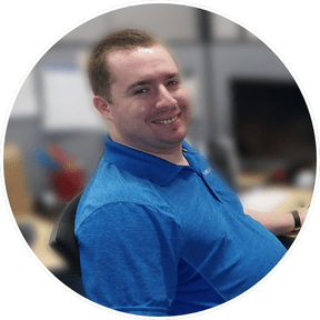 A circular photo of a man in a blue shirt, slightly facing away from the camera, smiling.