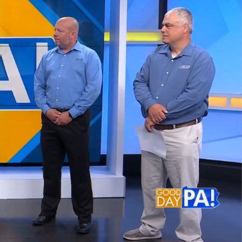 A square photo of two men on the set of a news set.