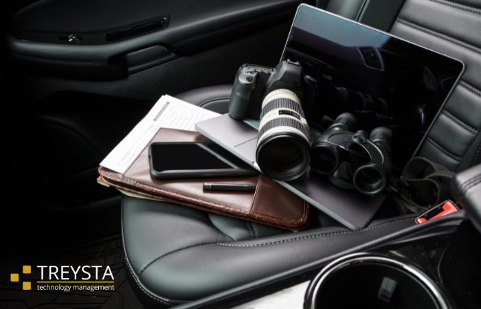 A dark photo of the interior of a car. On the seat is a binder, phone, camera, and laptop.